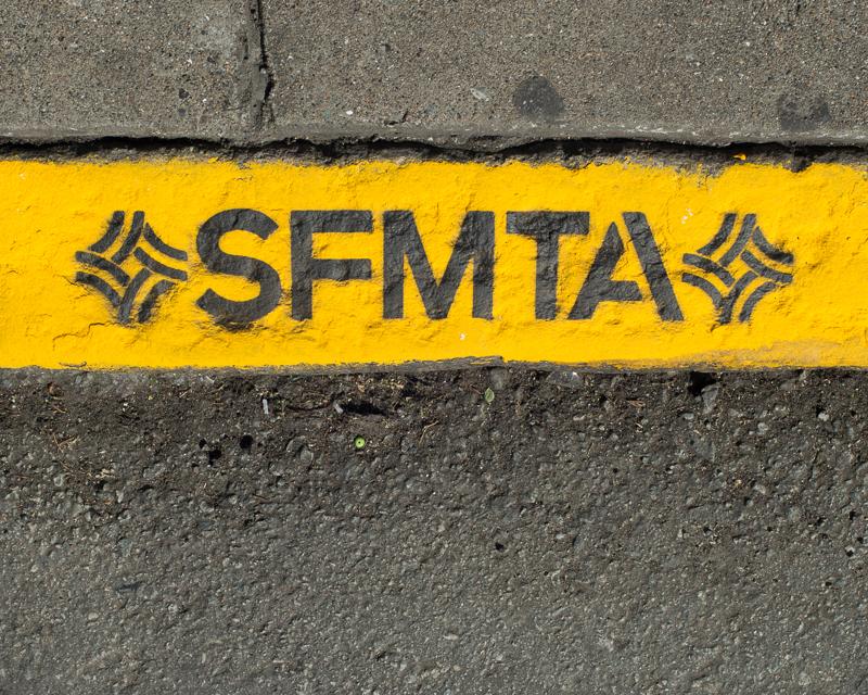 帶有字母的黃色彩繪路緣的詳細視圖 SFMTA 和 SFMTA 商標