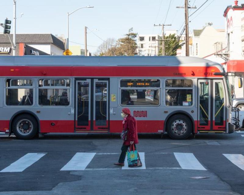 Image shows elderly crossing street with Muni bus in background