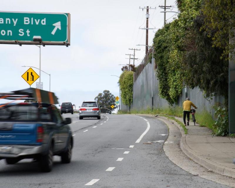 Bicyclist walking their bike on the sidewalk westbound on Alemany Blvd.