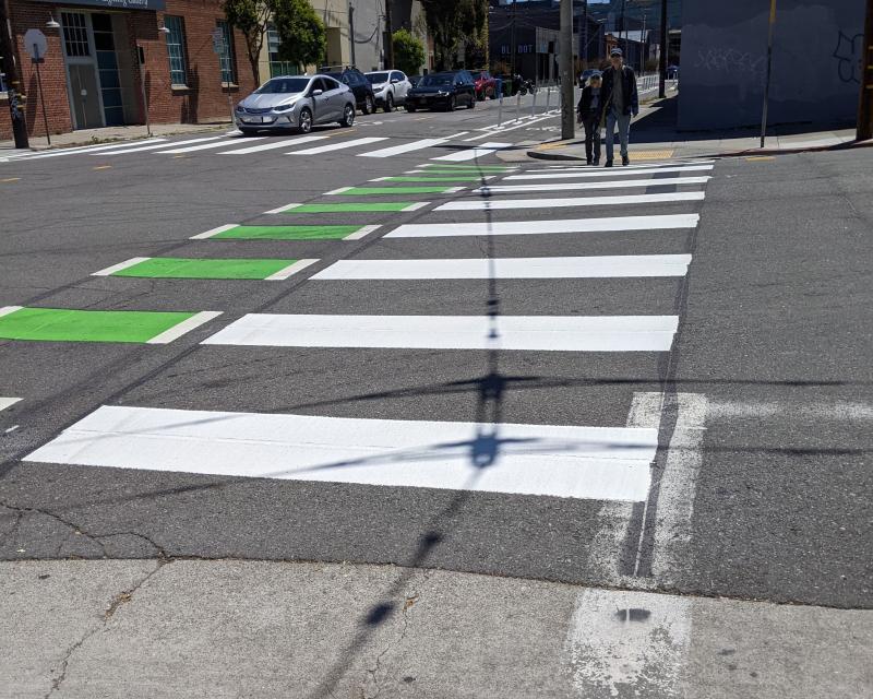 2 pedestrians crossing in a newly painted continental crosswalk next to a dashed green bike lane