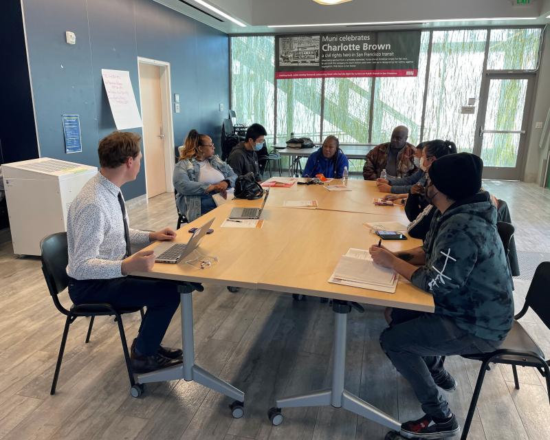 SFMTA staff and community partners sit at a table and chat in a conference room.