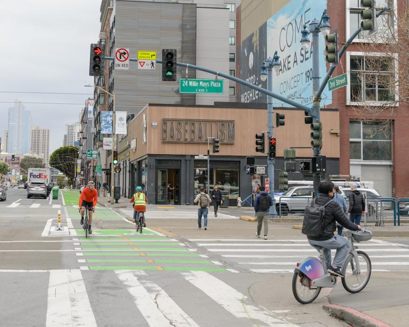 People use a two-way bikeway as others cross an intersection.