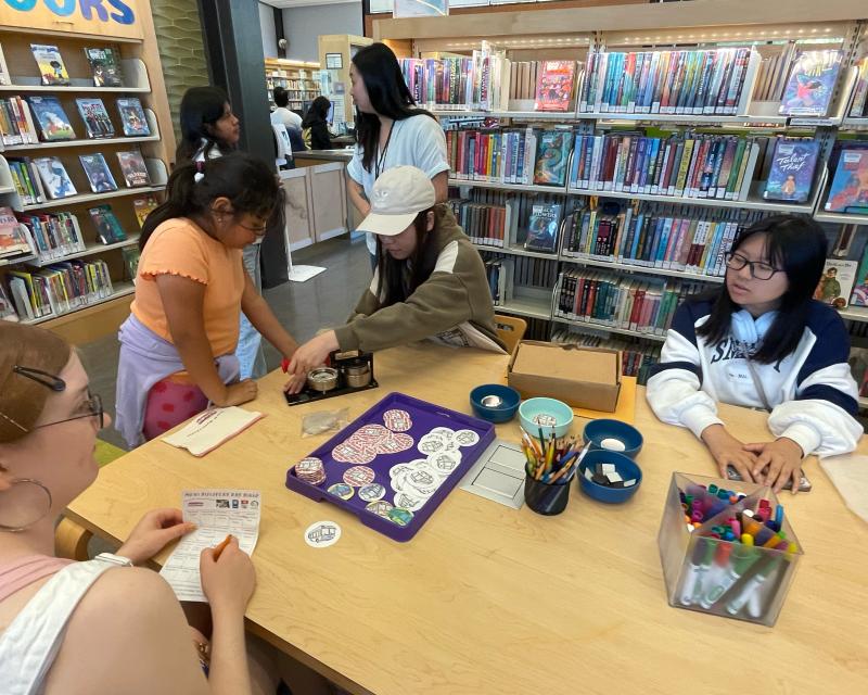 Young people sit at a table and make crafts in a library.