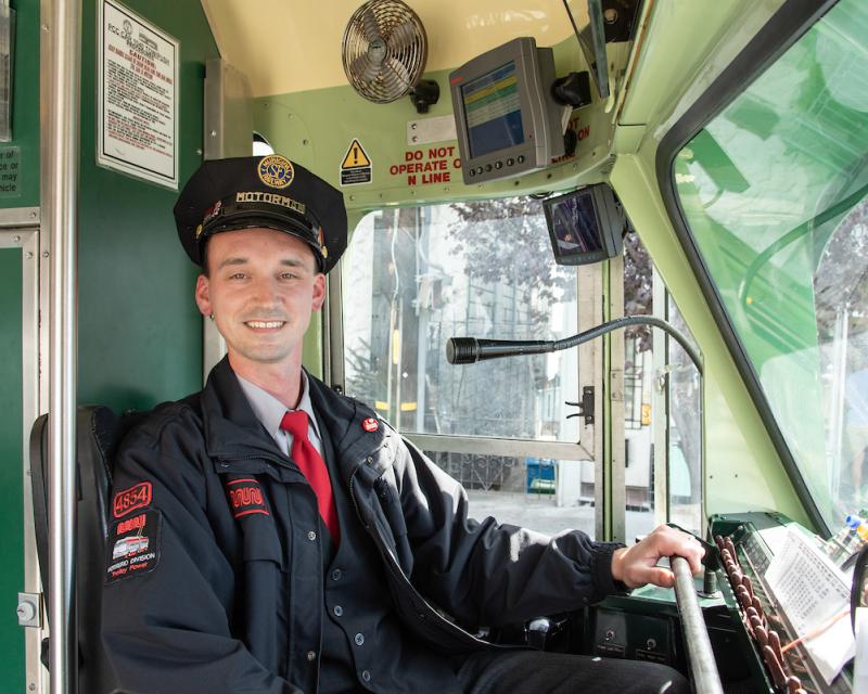 Mike Delia smiles broadly as he wears a vintage eight-point cap and sits in the operator’s seat of a historic streetcar.