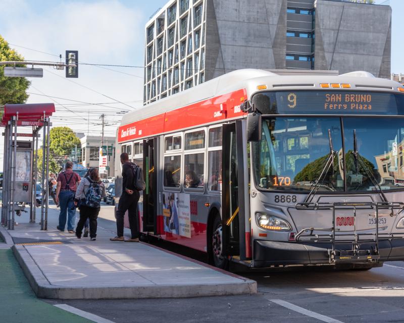 A photograph of Muni riders exiting the 9R San Bruno Rapid onto a boarding island on Potrero Avenue. 