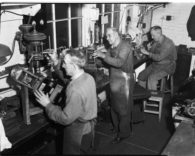 Black and white photo of shop mechanics repairing fare boxes for Muni in the 1940's.