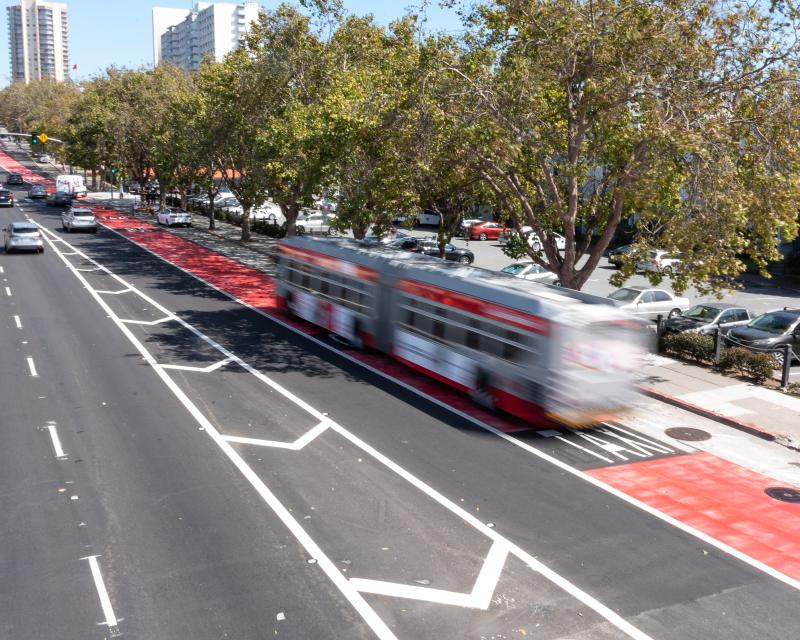 A bus uses a red transit-only lane near cars on a busy street