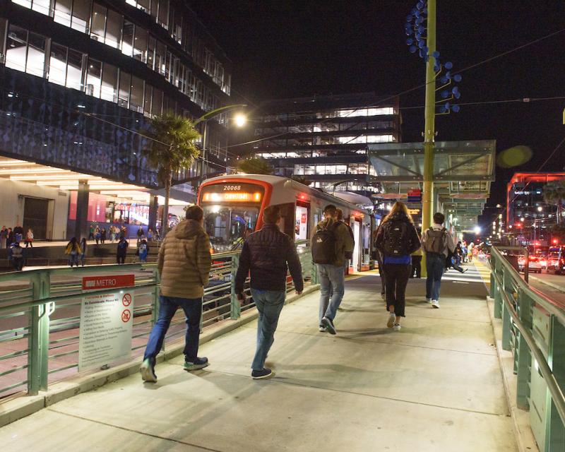 Several people walk up a ramp toward a T Third train that's waiting at a platform near Chase Center in the evening.