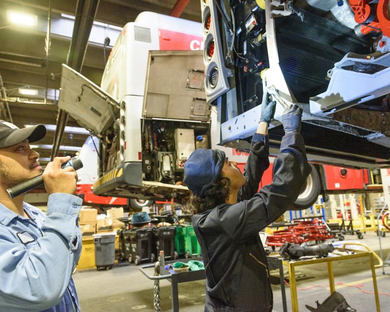 Two people inspect part of a Muni bus in one of the SFMTA's shops.