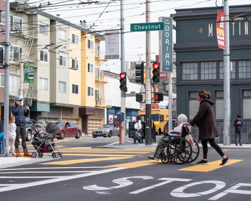 A person is pushing a senior in a wheelchair along a crosswalk at Chesnut Street. 