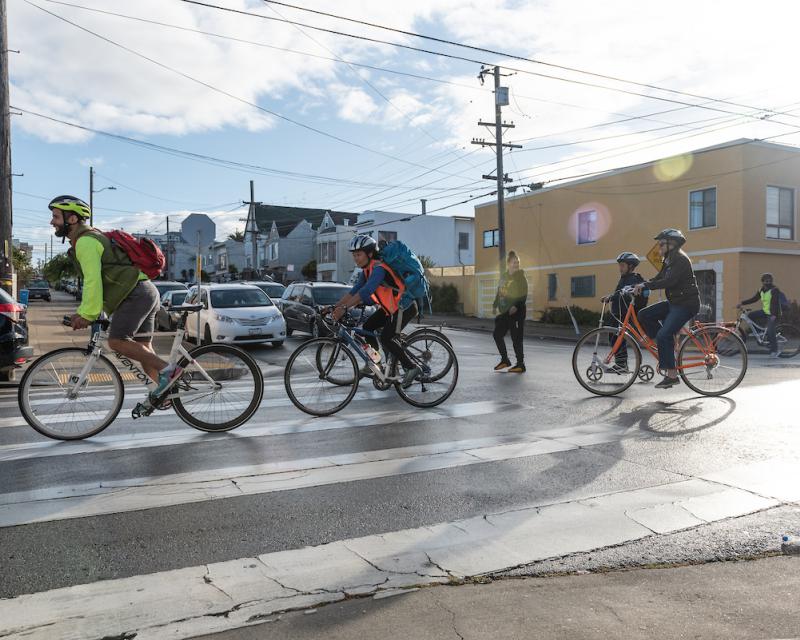 Several people bike across an intersection in a residential area.