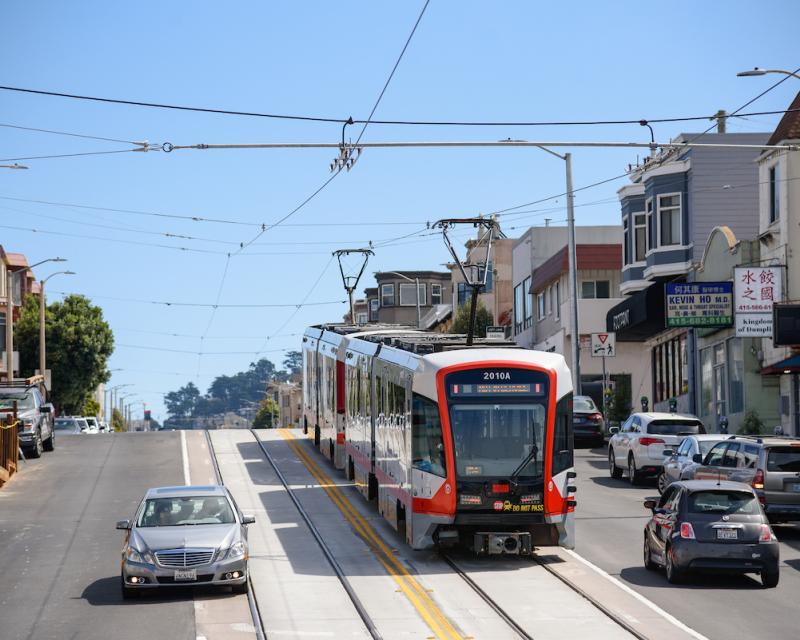 An L Taraval train heads down a hill as cars use nearby lanes.