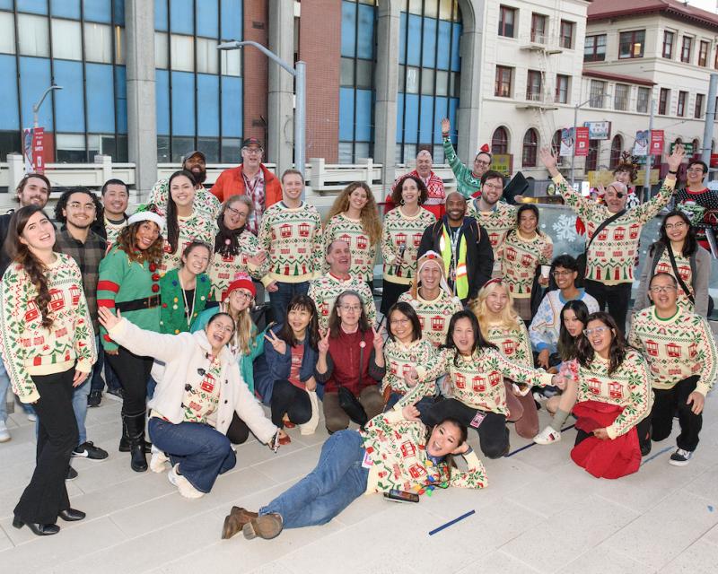 Several people wearing the Muni Icons of San Francisco sweater pose in front of buildings.