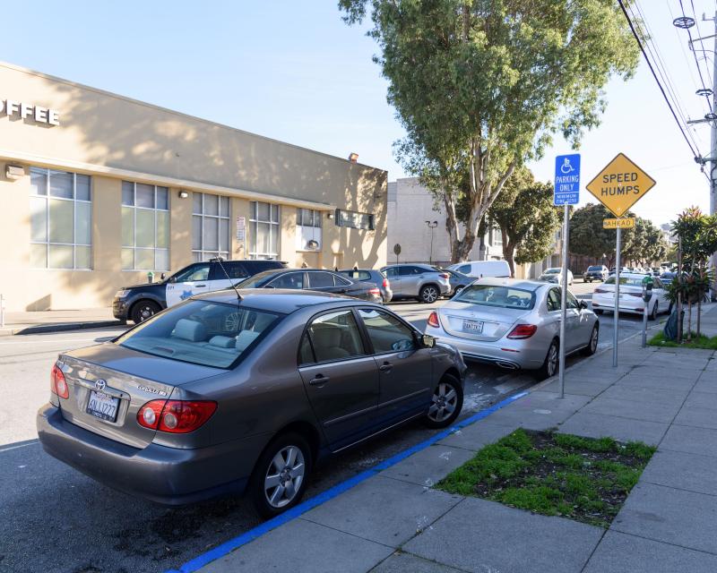 Car parked next to a curb that's painted blue. A sign also indicates that it's an accessible parking space.