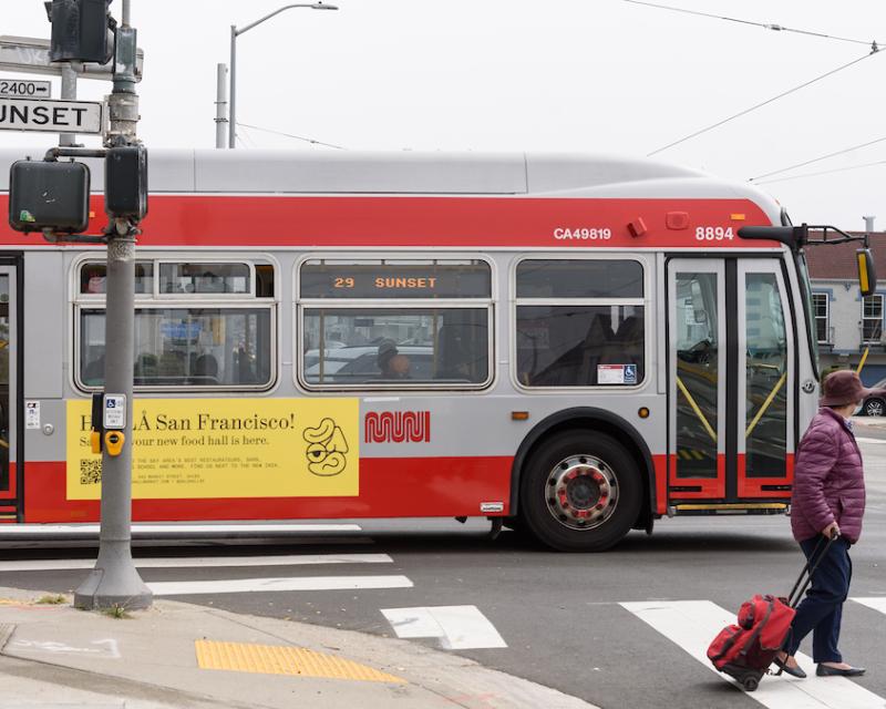 29 Sunset drives through an intersection. Nearby, a woman crosses the street.