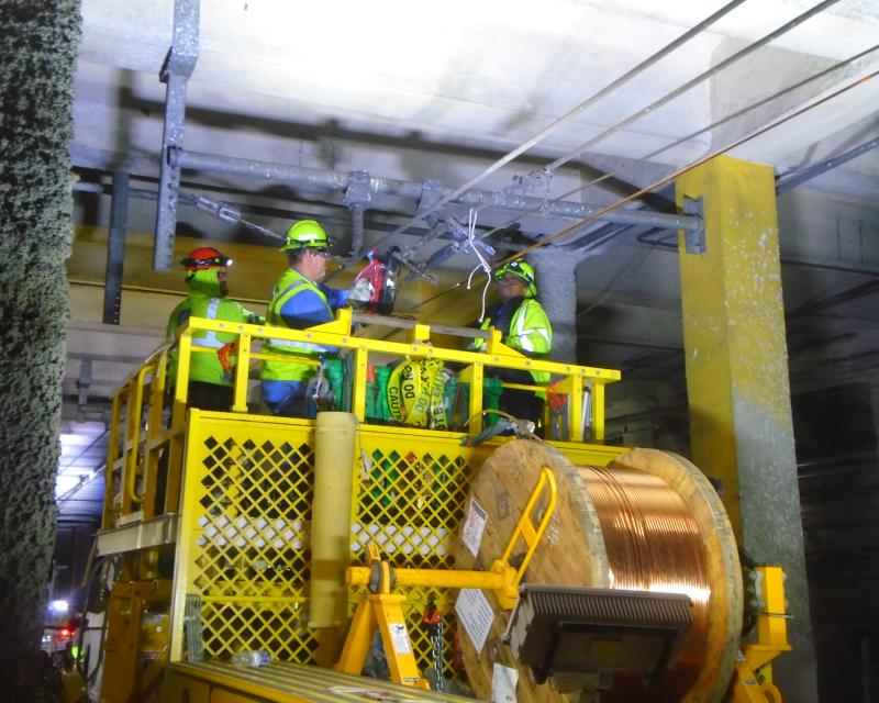 Crews wearing hard hats and yellow safety vests work on overhead lines.