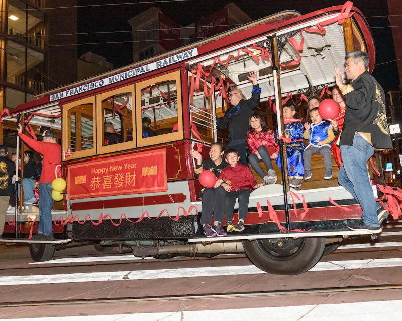 Several people ride a cable car that's decorated for the Chinese New Year Parade.