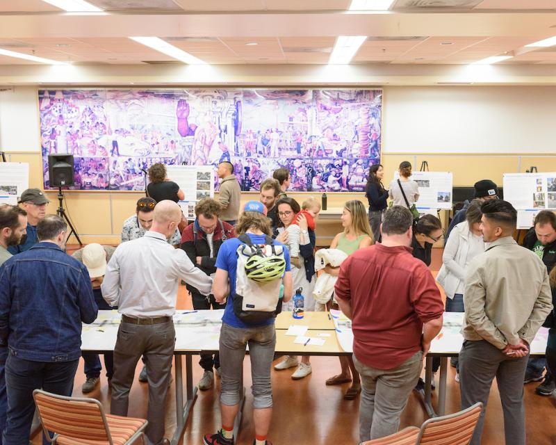 Several people stand around a table to review bikeway designs during a public event about the Valencia Bikeway Improvements project.