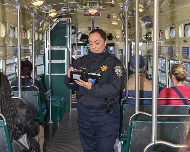 A woman standing on a transit vehicle with other people sitting on the vehicle. 