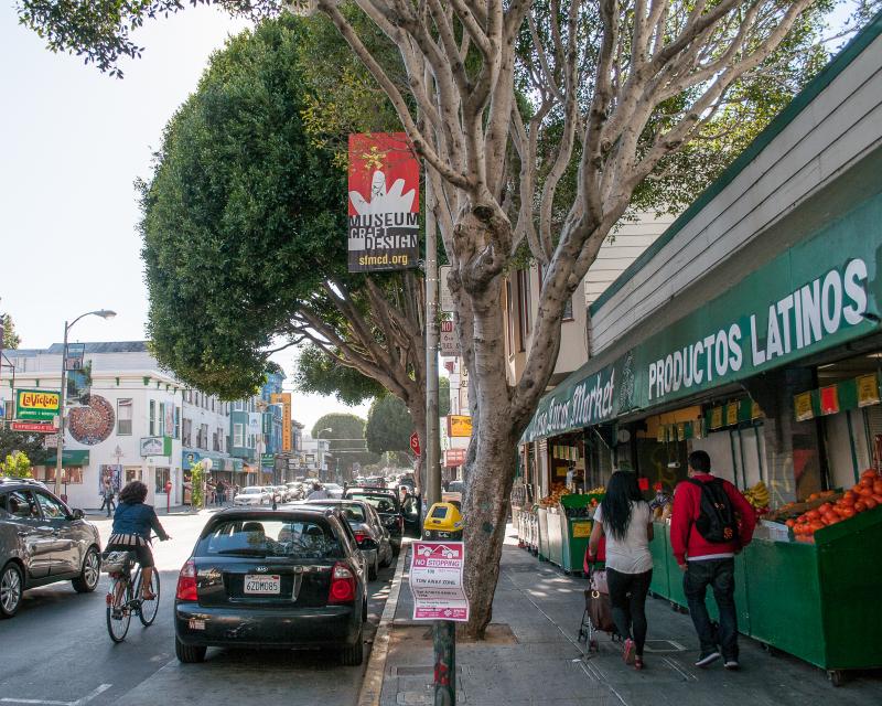 street scene in Mission district with produce market, people walking and cyclist