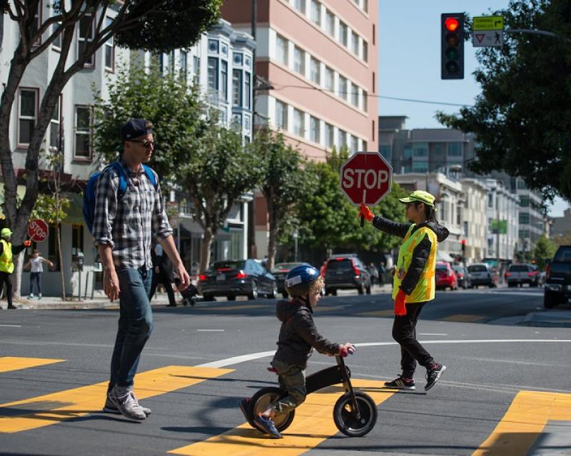 A crossing guard helping a father and son cross the street.