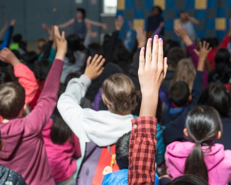 Kids in class raising their hands.