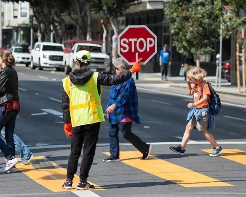 People crossing the street with the help of a crossing guard.