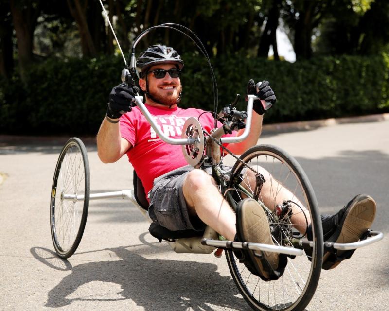(Image: Kurt, smiling, sits in a recumbent foot-pedal bike, holding the bike’s handlebars.)