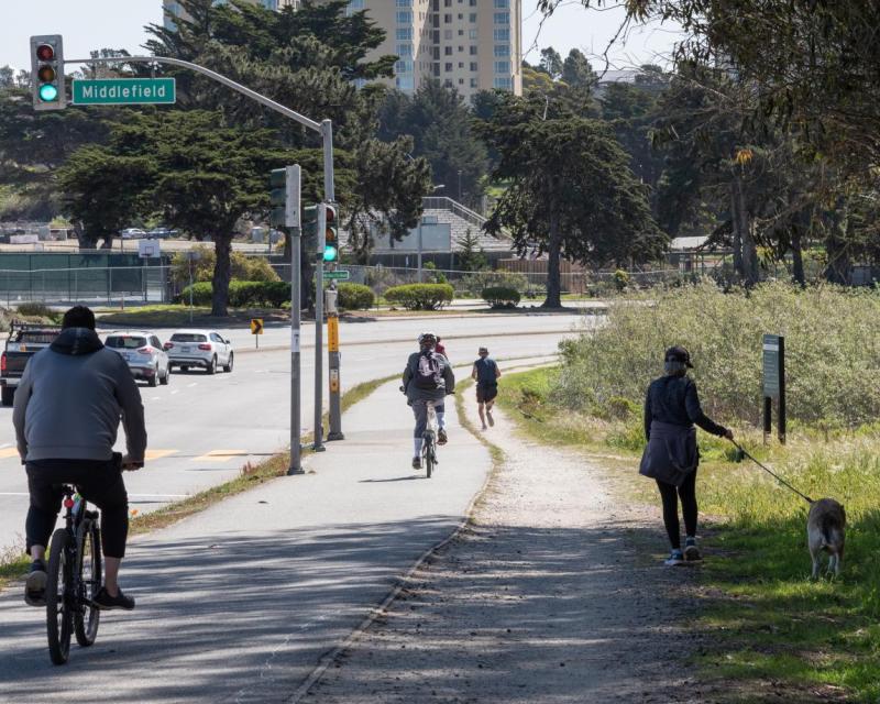 Photo of pedestrians, people on bicycles, and cars on Lake Merced Boulevard