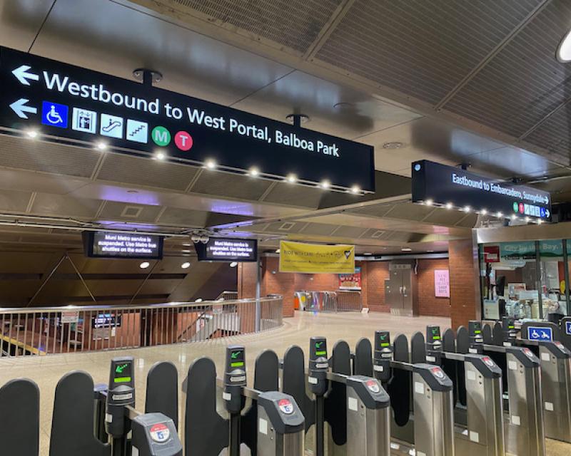 Photo of subway station fare gates with new overhead wayfinding signs depicting east, west directions and destinations for train