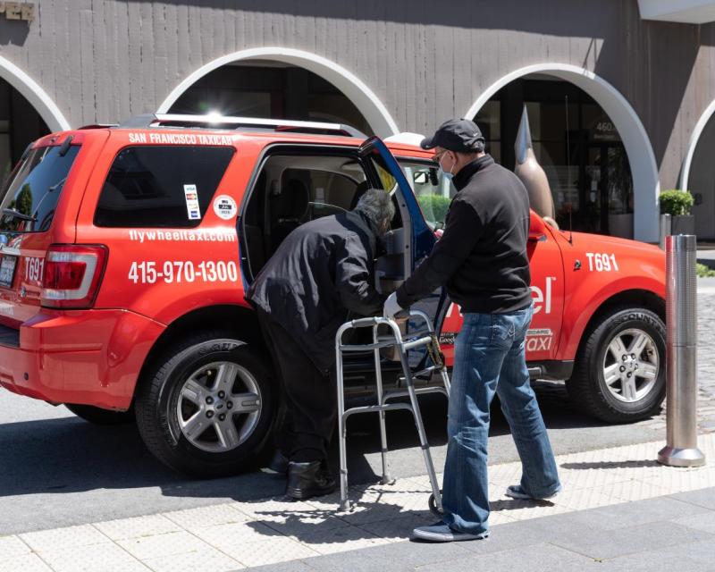 A taxi driver assists a passenger using a walker
