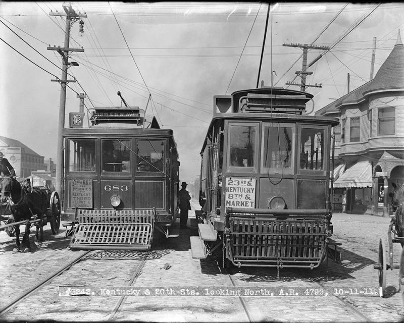 Two streetcars from 1911 shown with a person seen in the middle as well as a horse drawn carriage on the side.