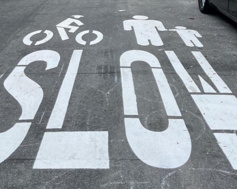 Slow Streets pavement markings in white show the outline of a cyclist, an adult and a child, and the word SLOW.