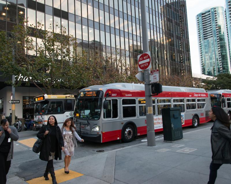 Personas cruzando una calle del centro frente a los autobuses Muni y Golden Gate Transit