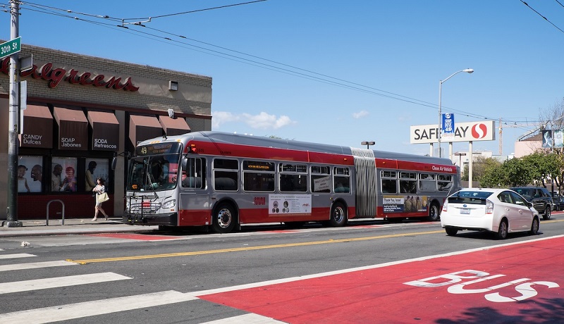 A Muni bus travels down a red transit-only lane on Mission Street at 30th Street as cars travel in the adjacent traffic lanes.