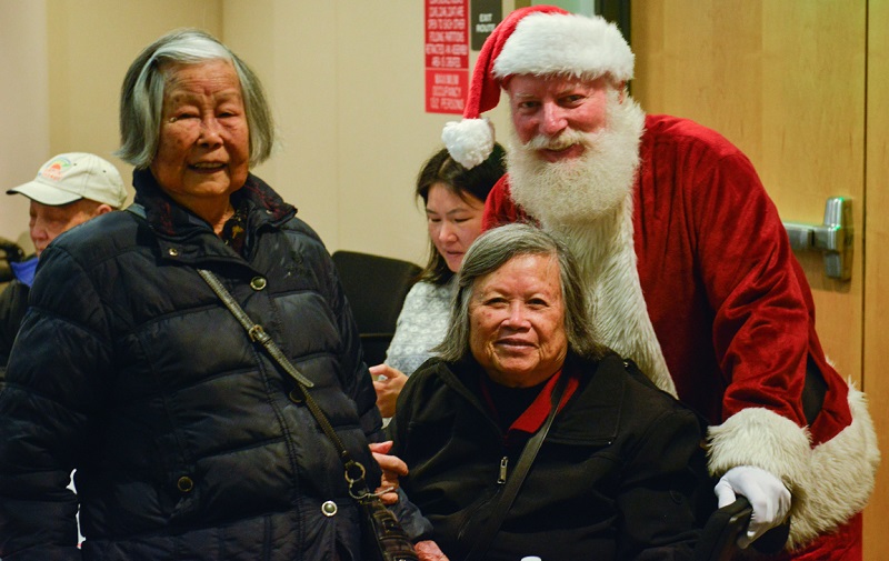 Santa Claus stands next to two women attending the Cable Car Seniors Luncheon.